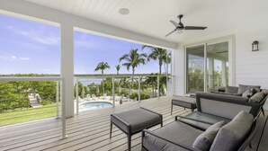 A spacious balcony with a pool, outdoor furniture, and a view of palm trees and water.