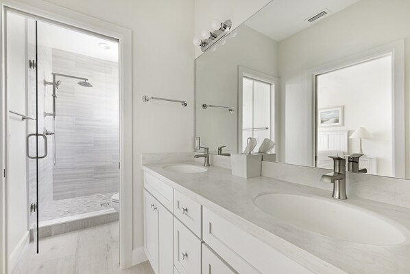 Un baño moderno con cabina de ducha de vidrio, dos lavamanos y un espejo grande.