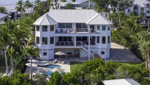 A two-story house with a pool, surrounded by palm trees and a view of the ocean.