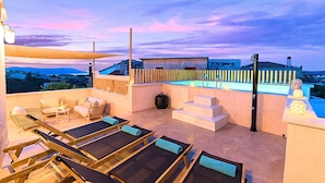 Une terrasse sur le toit avec des chaises longues, une piscine et une vue sur le paysage urbain au crépuscule.