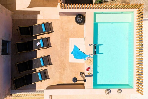 An aerial view of a pool area with lounge chairs, a sun umbrella, and a small table with a hat and sunglasses. - Villa Mirage - Private Plunge Pool & Views (Kournás)