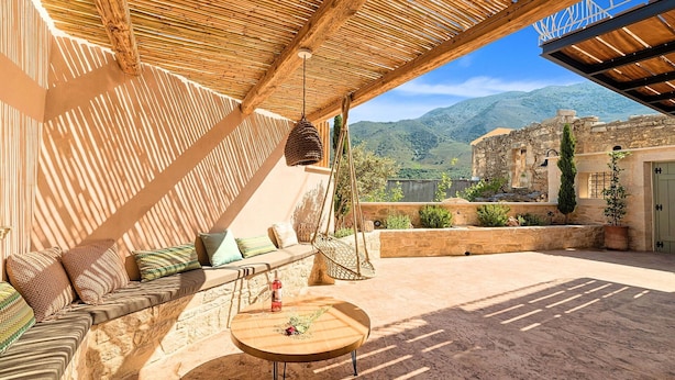 Un espace extérieur accueillant, avec une table en bois, des coussins et une vue sur un bâtiment historique en pierre.