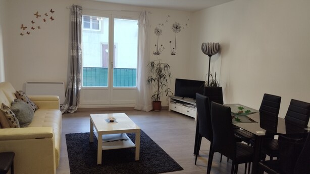 A living room with a sofa, coffee table, TV, and dining area with chairs and a table.