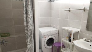 A compact bathroom with a shower, a washing machine, and a sink.
