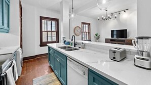 A modern kitchen with a large island, built-in appliances, and a dining area with a TV. - Historic Loft in the Heart of Downtown (Galveston)