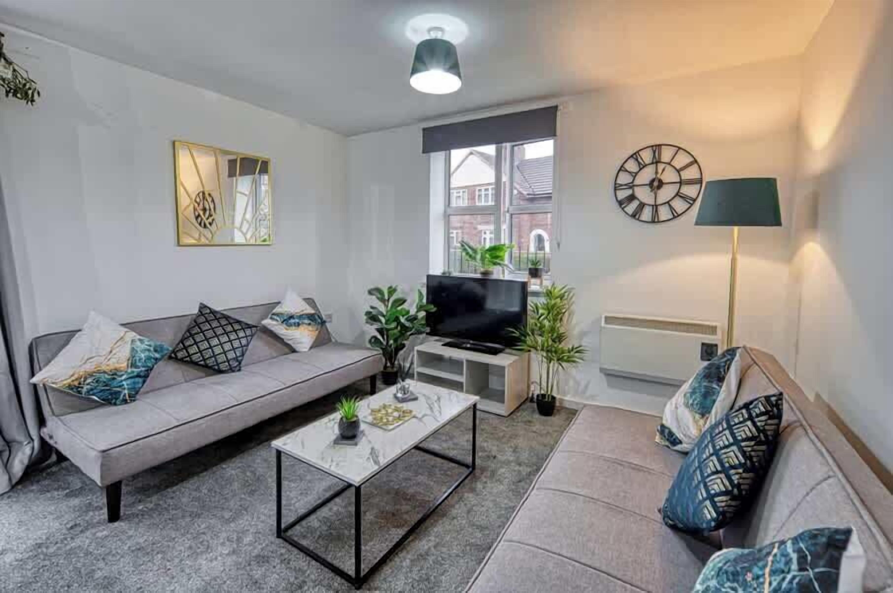 Un salon moderne avec un canapé gris, une table basse, un téléviseur et une lampe.