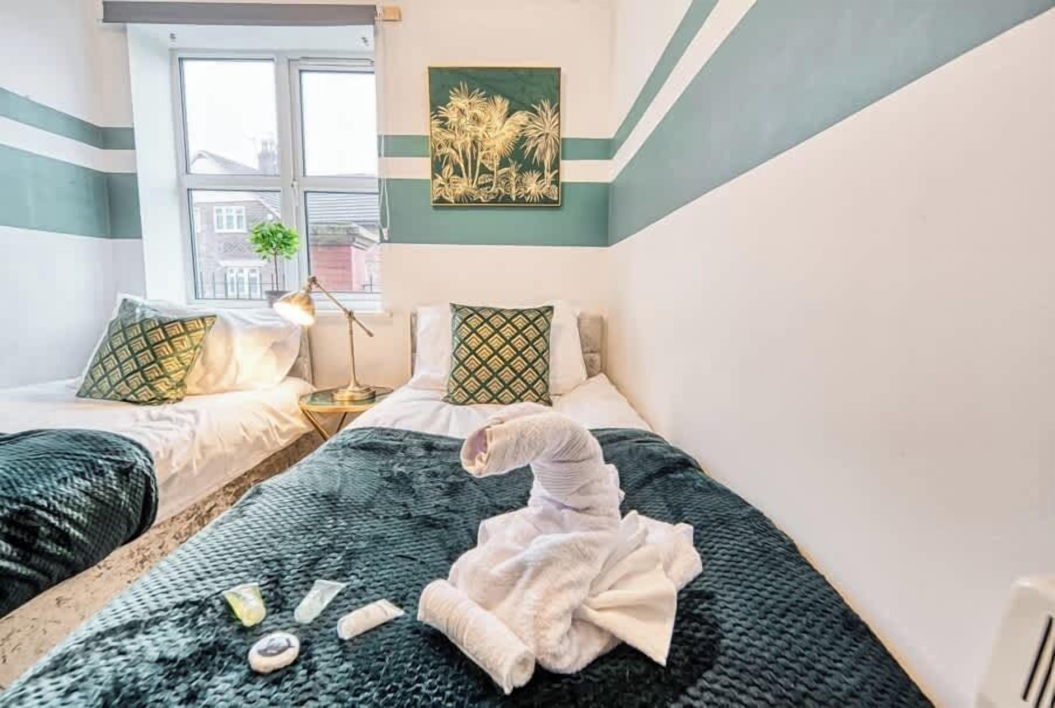 Habitación de hotel con dos camas, una ventana, un cuadro y una mesita de noche con lámpara.