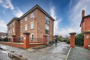 A two-story brick apartment building with a gated entrance and a paved driveway. - The Sale Luxe | Captivating 2BR w/ Secured Parking (Manchester)