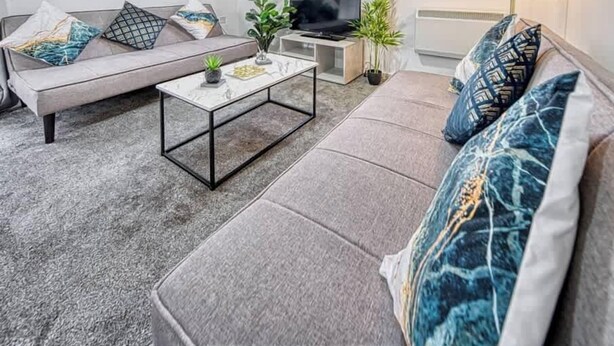 Ein modernes Wohnzimmer mit einem grauen Sofa, einem Couchtisch und einem Fernseher.