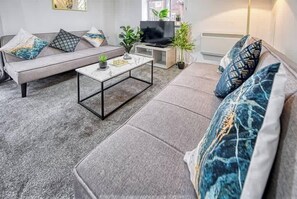Uma sala de estar moderna com um sofá cinza, uma mesa de centro e uma televisão.