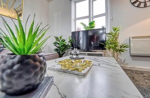 A modern living room with a marble table, a television, and various plants. - Sale Modern Luxe 2BR - Your Work Stay W/ Parking (Manchester)