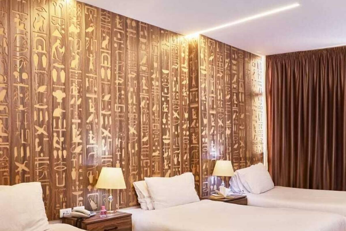 Habitación de hotel con dos camas, paneles de madera con jeroglíficos e iluminación moderna.
