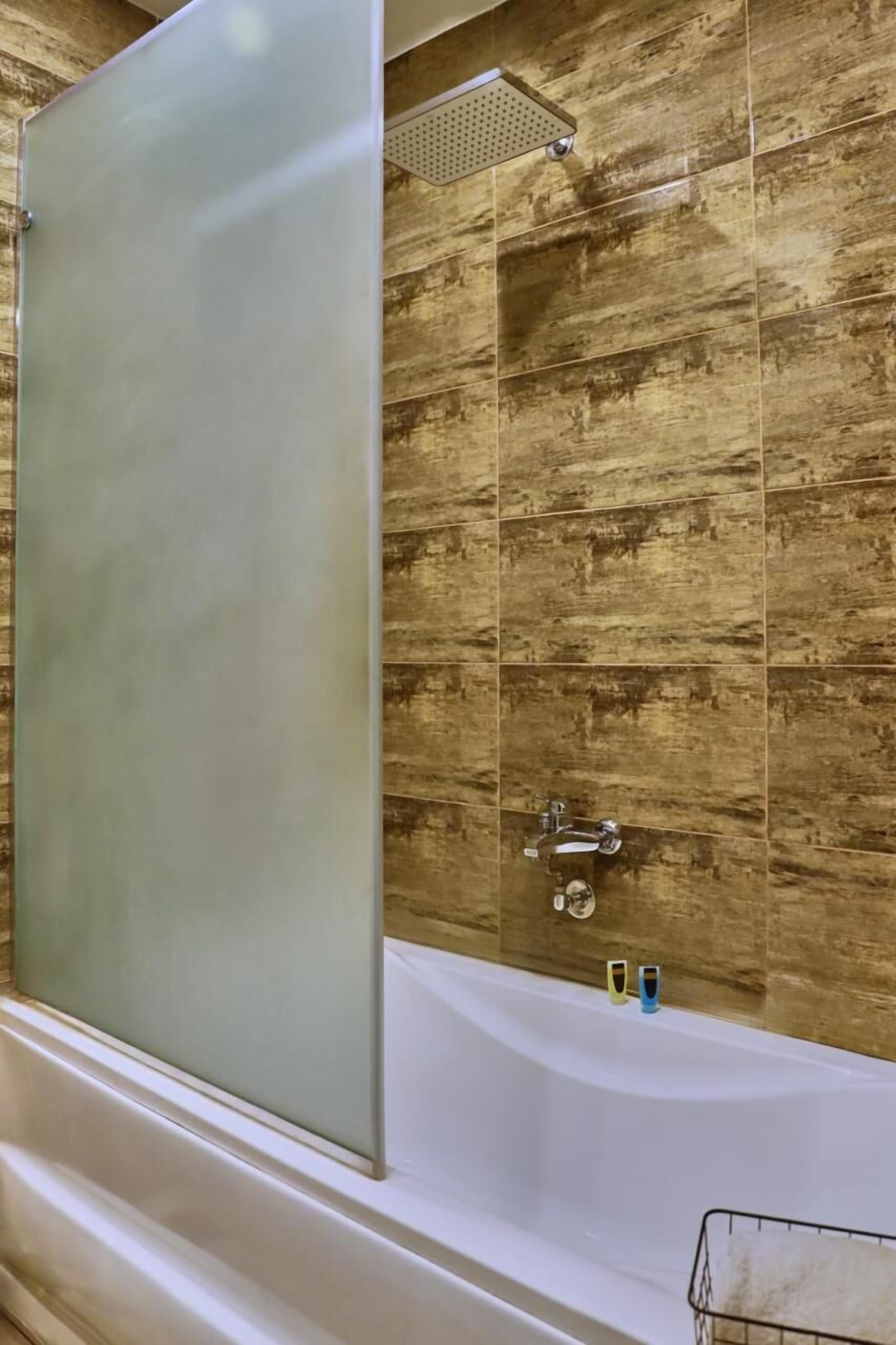 A bathroom with a bathtub, a shower enclosure, and a tiled wall.