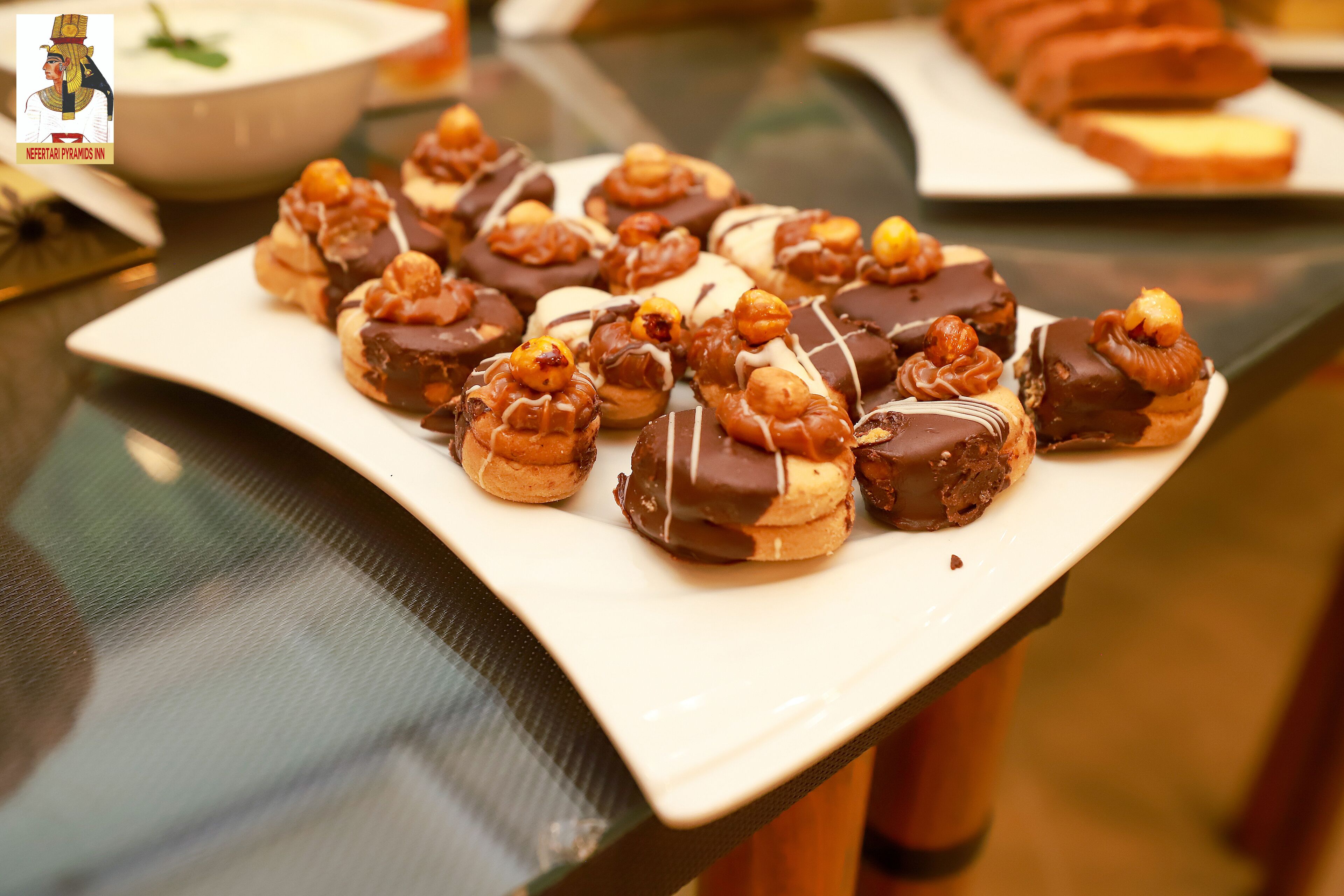 Un plato con varios pasteles y dulces, algunos cubiertos de chocolate y otros con nueces, sobre un plato blanco rectangular.