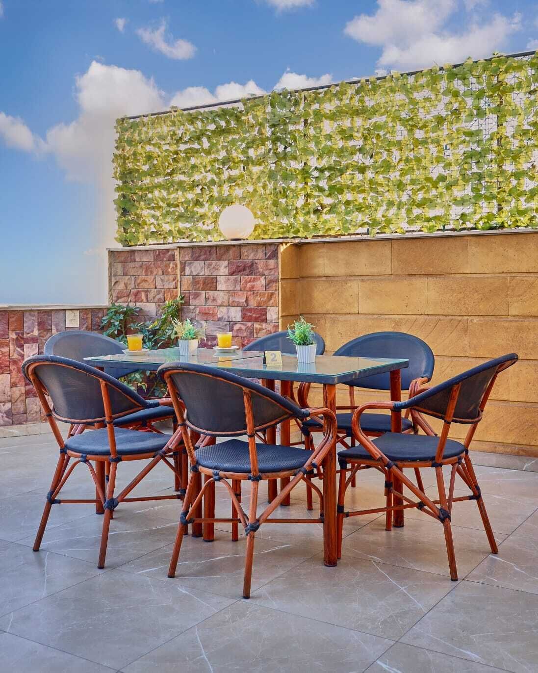 An outdoor dining area with a table and chairs, a brick wall, and a green leafy wall.