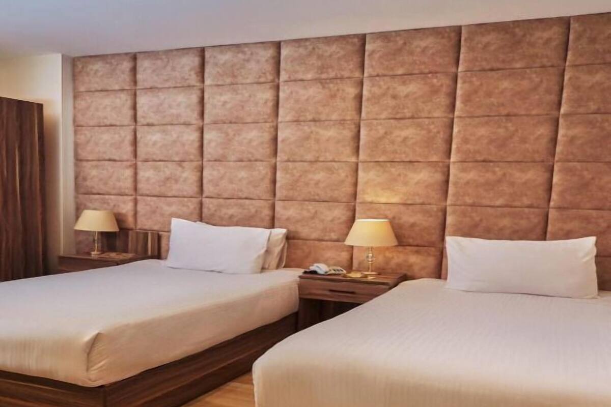 Habitación de hotel con dos camas, cabecero de madera, lámparas de noche y suelo de madera.