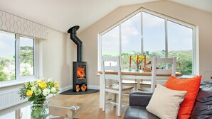 A cozy living room with a fireplace, a sofa, a dining table, and a view of the outdoors.