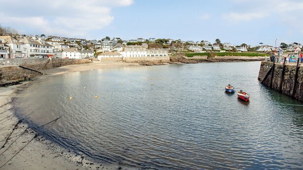 A coastal town with a calm harbor, stone walls, and a sandy beach.
