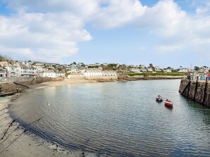 Un pueblo costero con un puerto tranquilo, muros de piedra y una playa arenosa.