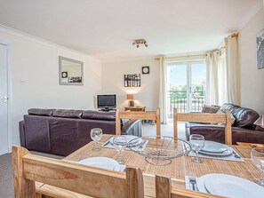 Un coin repas avec une table dressée pour quatre personnes, un canapé, un téléviseur et un balcon avec des rideaux.