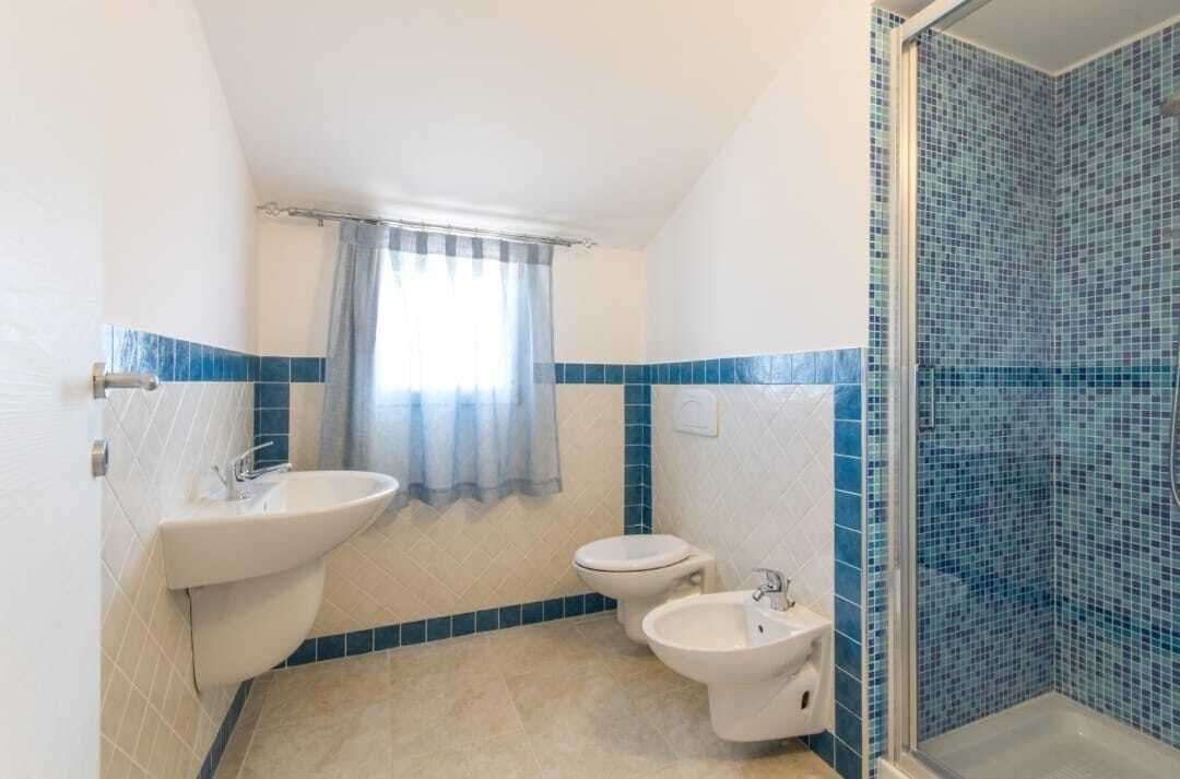 Une salle de bain équipée d’un lavabo, de toilettes, d’un bidet et d’un espace douche aux carreaux de mosaïque bleus.