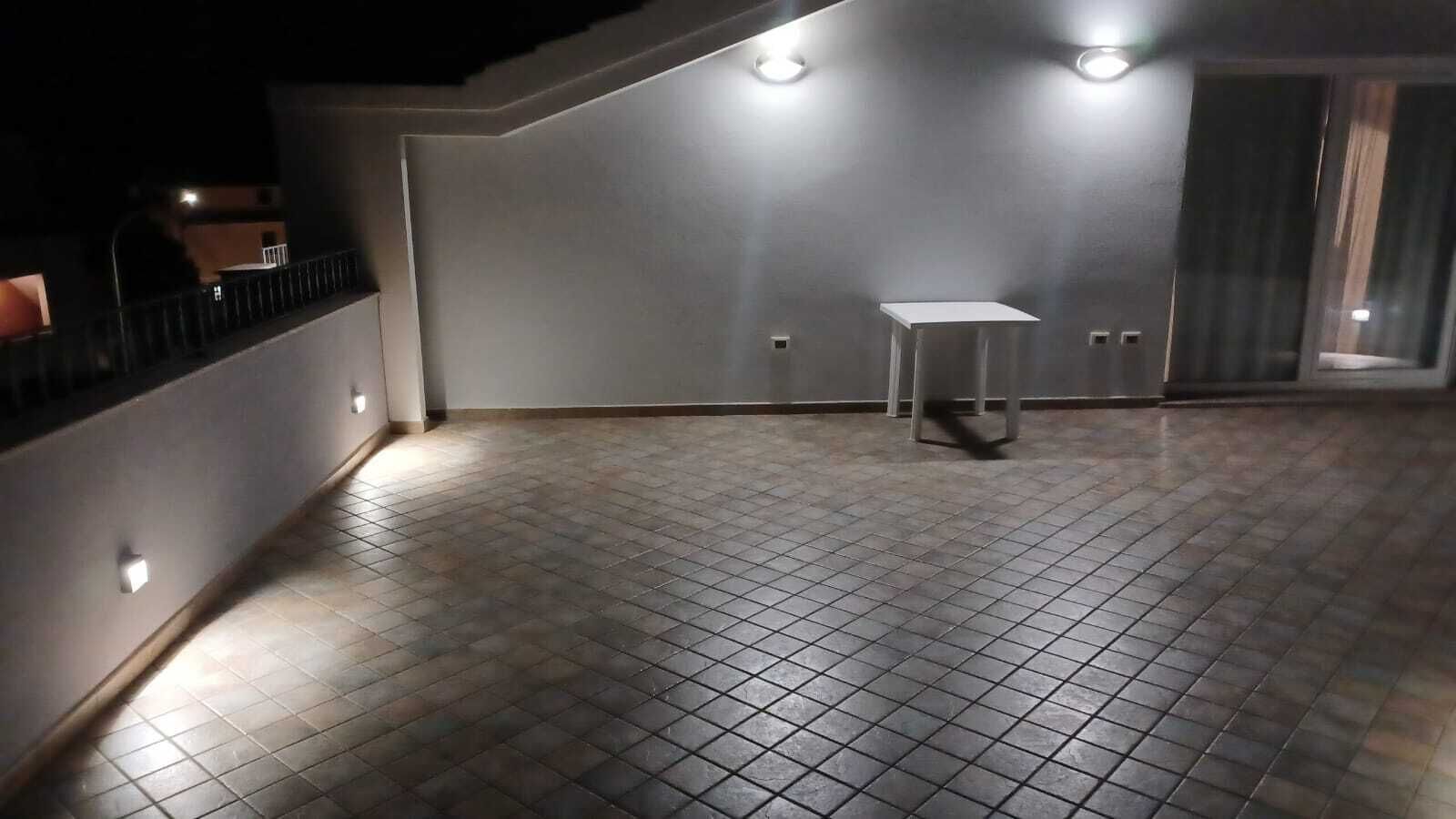 Ein mit Fliesen ausgelegter Patio-Bereich mit einem kleinen Tisch und einem Stuhl, umgeben von Mauern mit eingelassener Beleuchtung.