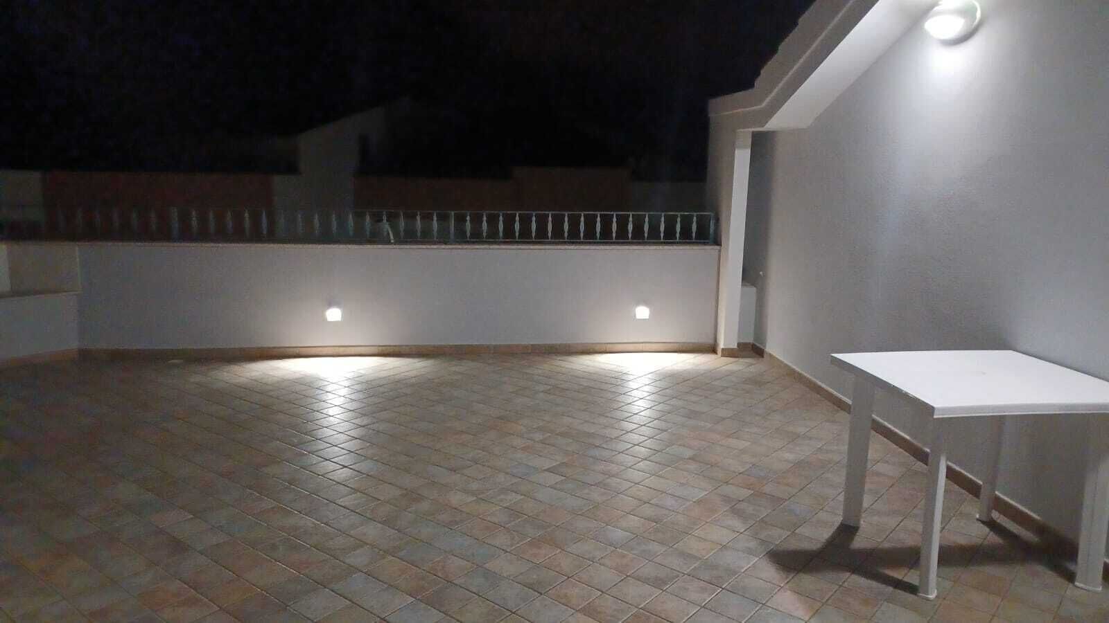 An outdoor patio area with tiled flooring, a white table, and two wall-mounted lights.