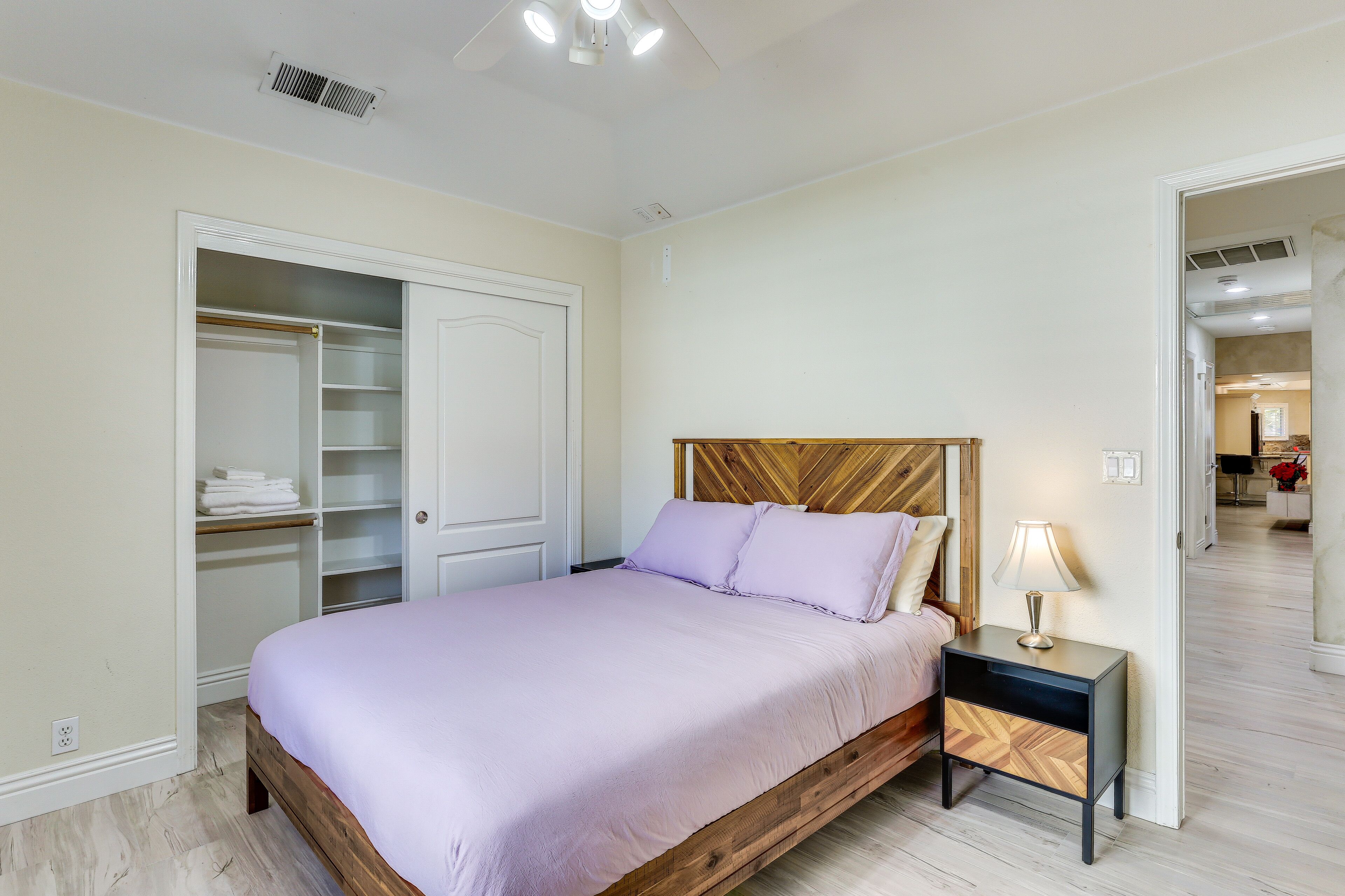 Un dormitorio con cama, mesita de noche, armario y una puerta que da a otra habitación.