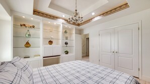Una camera da letto con un letto grande, scaffali a muro con oggetti decorativi, un lampadario e porte bianche.