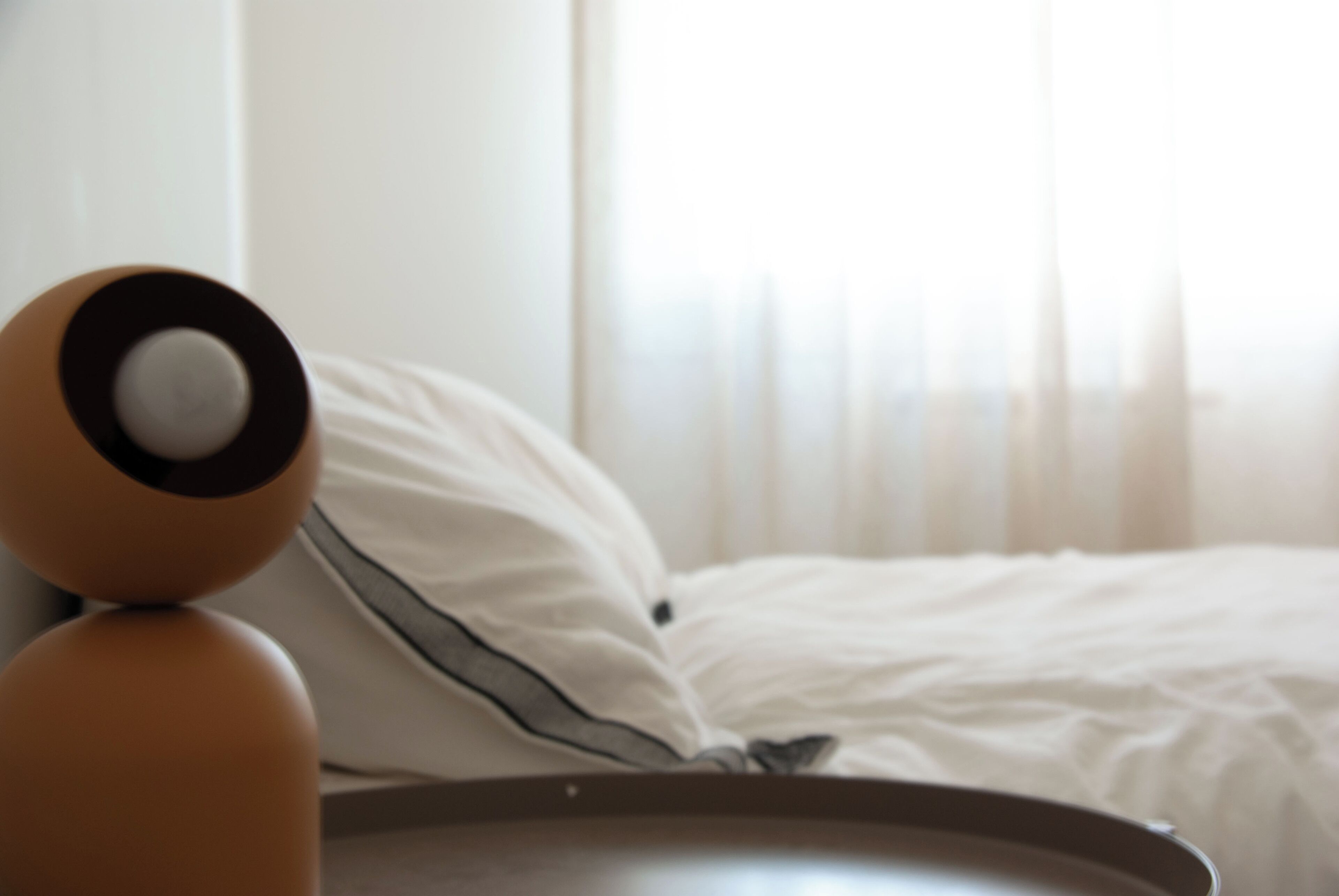 Una cama con ropa de cama blanca y una almohada con una banda negra.