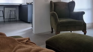 A modern room with a green armchair, a small ottoman, a desk with a chair, and a large window. - Florence Design Apartment (Firenze)