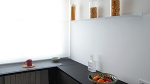 A kitchen counter with a bowl of fruit, a red mug, and three glass jars on a white shelf. - Florence Design Apartment (Firenze)