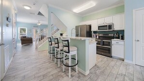 A modern kitchen with a central island, white cabinets, stainless steel appliances, and a light green accent wall. - Pet Friendly - 3 BR 3.5 BA  Pool  Garage 2 Balconies  2 blocks to Beach!! (Corpus Christi)