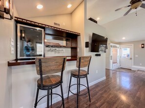 A kitchen area with wooden bar stools, a built-in wine rack, and a large flat-screen TV mounted on the wall. - 3Bed/2Bath Home, Brick Patio, Large Deck & Fenced In - Near Downtown! (Cedar Falls)