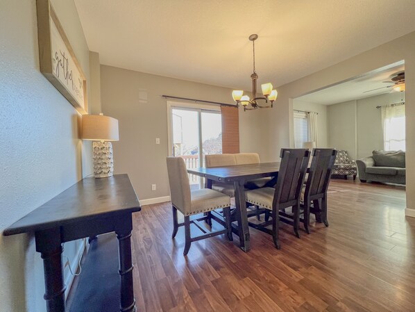 A dining area with a dark wooden table and chairs, a chandelier, and a view of the outdoors through a sliding glass door. - 3Bed/2Bath Home, Brick Patio, Large Deck & Fenced In - Near Downtown! (Cedar Falls)