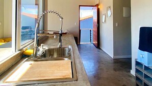 A modern kitchen with a stainless steel sink, wooden countertop, and hanging pendant lights. - RiqueHouse Hidro churrasqueira a 500 m (Marica)