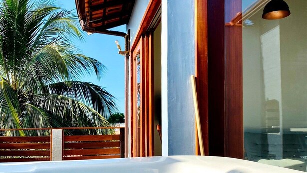 A hot tub outside a building with a wooden roof and a palm tree in the background. - RiqueHouse Hidro churrasqueira a 500 m (Marica)