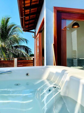A hot tub outside a building with a wooden roof and a palm tree in the background. - RiqueHouse Hidro churrasqueira a 500 m (Marica)