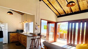 A spacious kitchen with a large island, wooden bar seating, and a high ceiling with natural light. - RiqueHouse Hidro churrasqueira a 500 m (Marica)