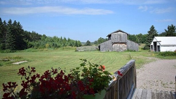 A rural landscape with a wooden barn and a white building, surrounded by greenery and a clear sky. - NEW LISTING - FARMHOUSE --VERY CLOSE TO SNOWMOBILE TRAILS - VERY PRIVATE (Brimley)