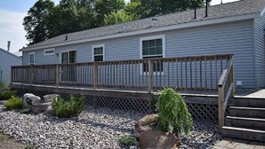 A single-story mobile home with a wooden deck and a small garden area with rocks and plants. - NEW LISTING - FARMHOUSE --VERY CLOSE TO SNOWMOBILE TRAILS - VERY PRIVATE (Brimley)