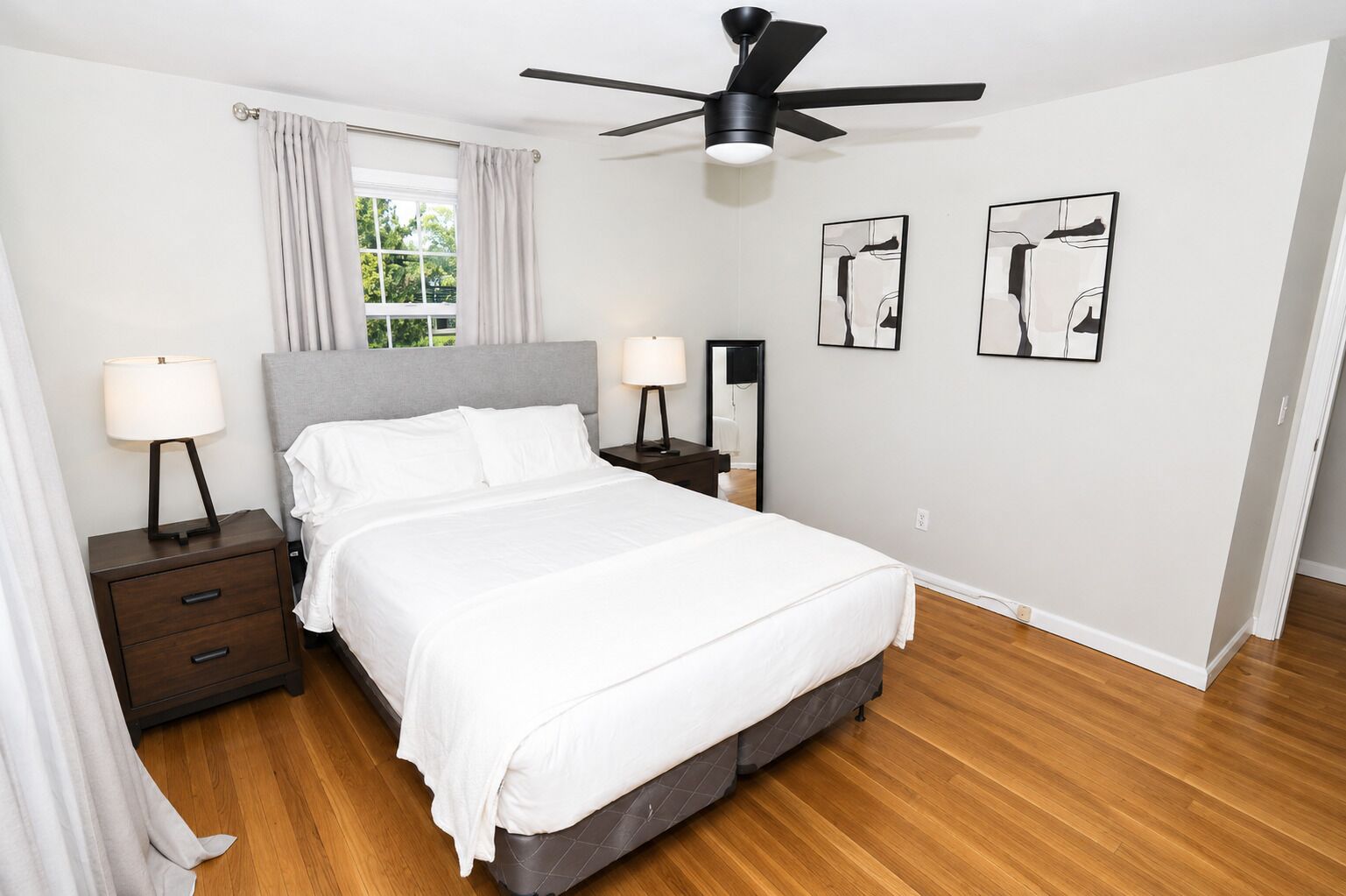 A bedroom with a bed, nightstands, a ceiling fan, and artwork on the walls.