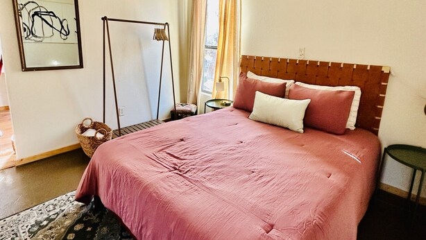 Una camera da letto con un letto grande, una ventola a soffitto, una finestra con tende, un comodino e un tappeto.