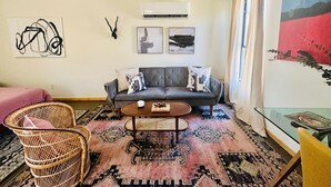 Un soggiorno con un divano grigio, due cuscini decorati, una poltrona in vimini, un tavolino da caffè e un tavolo in vetro con riviste.