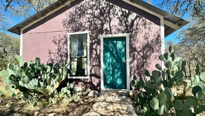 A small house with a teal door and windows, surrounded by cacti. - Hill Country Bungalow at Mosaic (San Marcos)