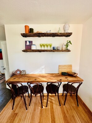 A wooden dining table with four chairs, a white wall with two rustic shelves, and a wooden headboard. - Hill Country Bungalow at Mosaic (San Marcos)