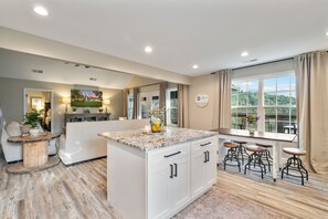 A modern kitchen with a central island, bar stools, and a large window offering a view of greenery.