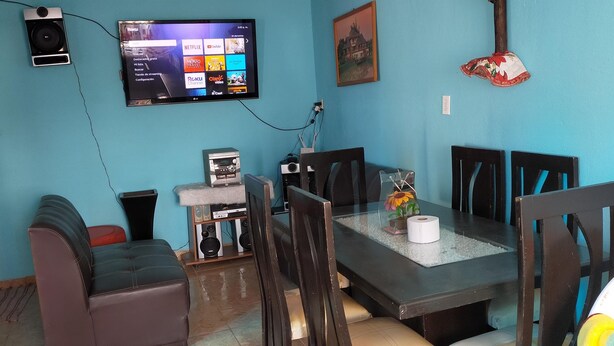 A dining area with a table, chairs, a television mounted on the wall, a small speaker, and a decorative item on the table.