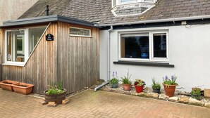 Een huisje met een houten gevel, een klein terras en een tuin met bloempotten.