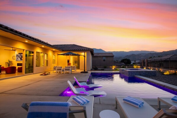 Un área de piscina moderna al aire libre con sillones reclinables y sombrillas, un patio bien iluminado y vistas a montañas distantes.